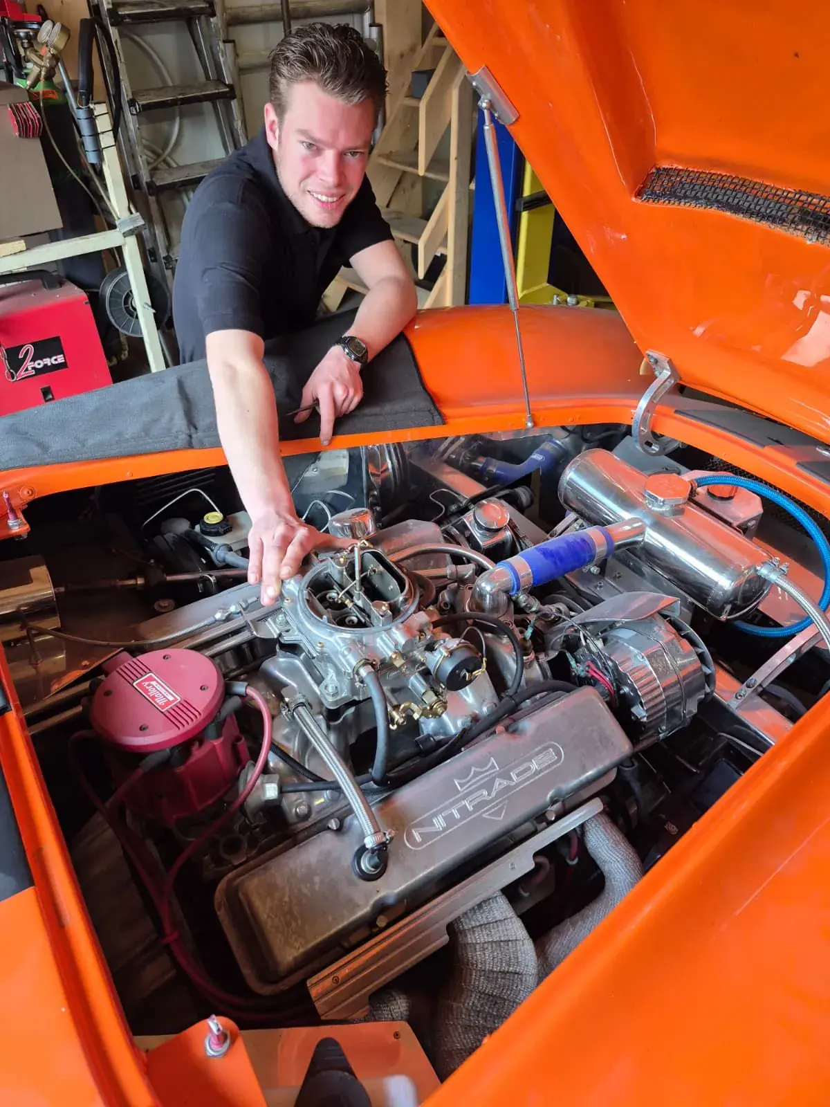 Symen Benima wijst naar de carburateur in de motorruimte van een oranje klassieker